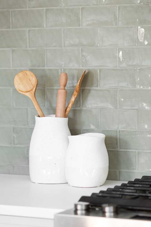 sage green glazed subway tile backsplash in kitchen with wooden utensils